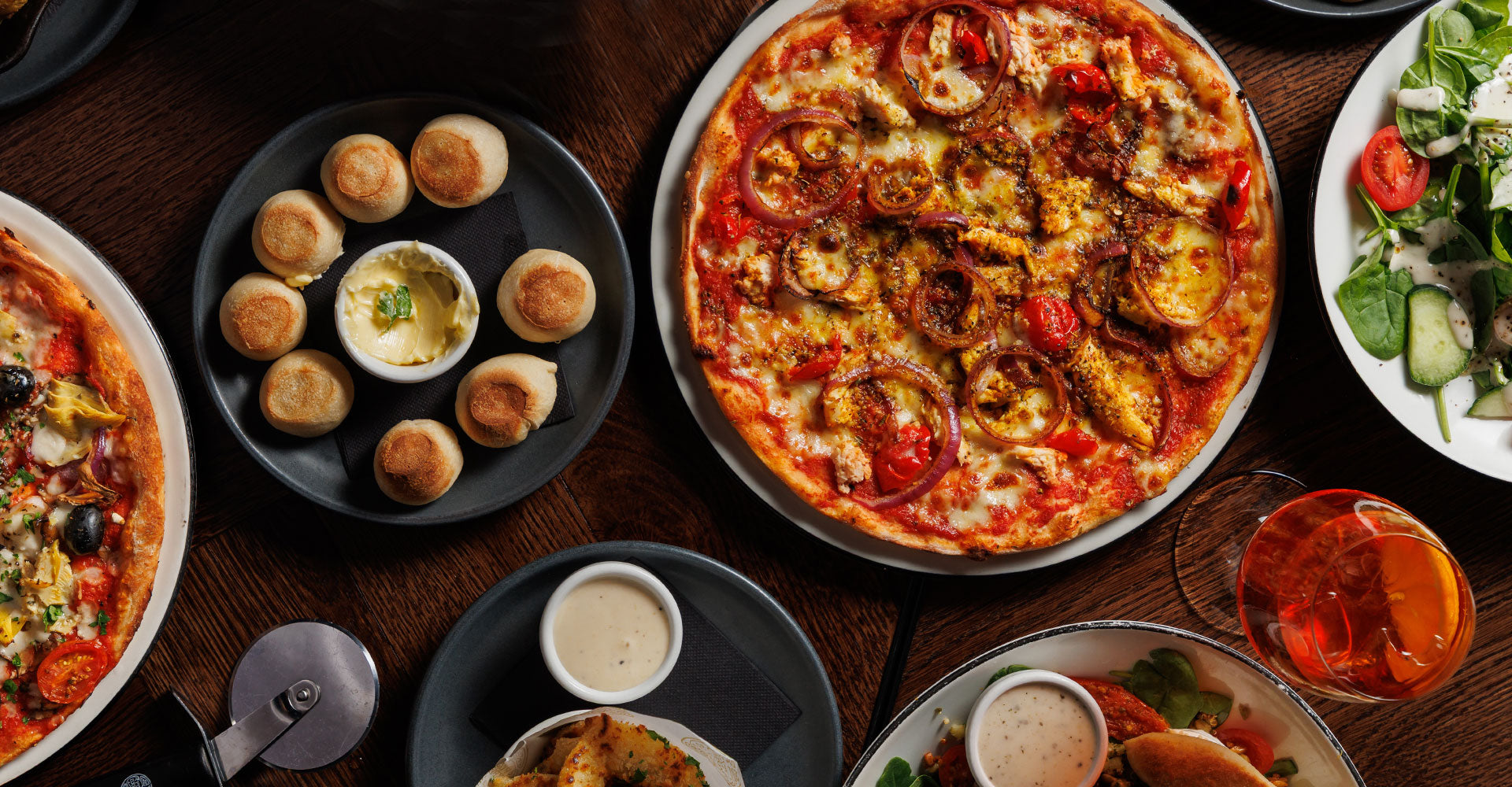 Assorted pizzas, bread rolls, and side dishes on a wooden table