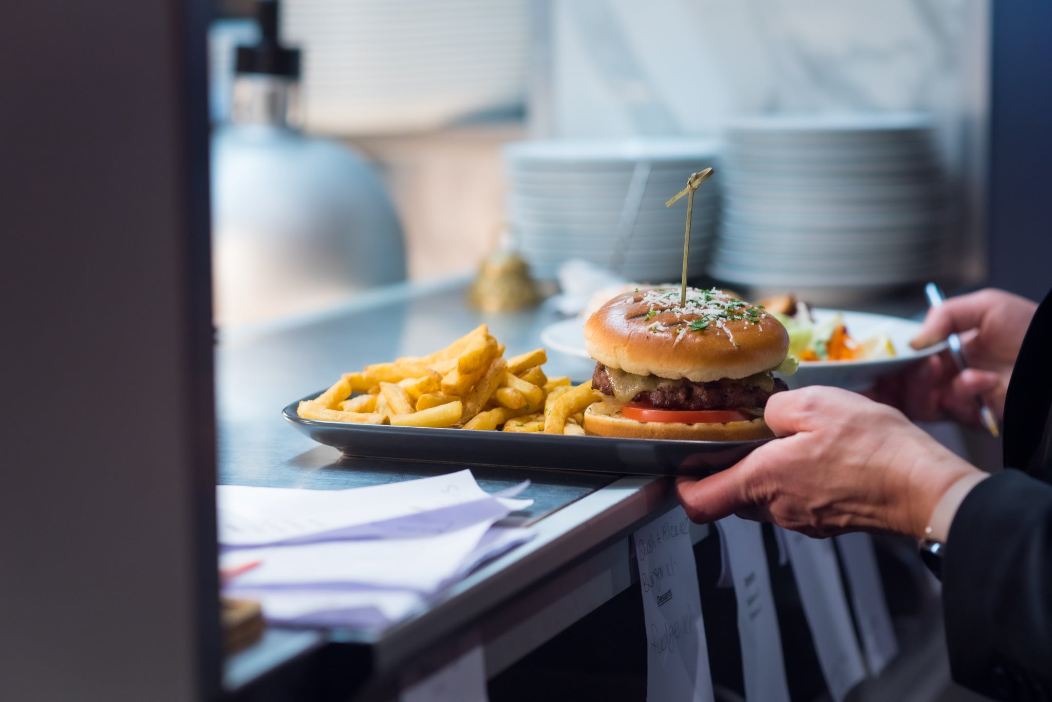 Person holding a plate with a burger and fries in a kitchen setting
