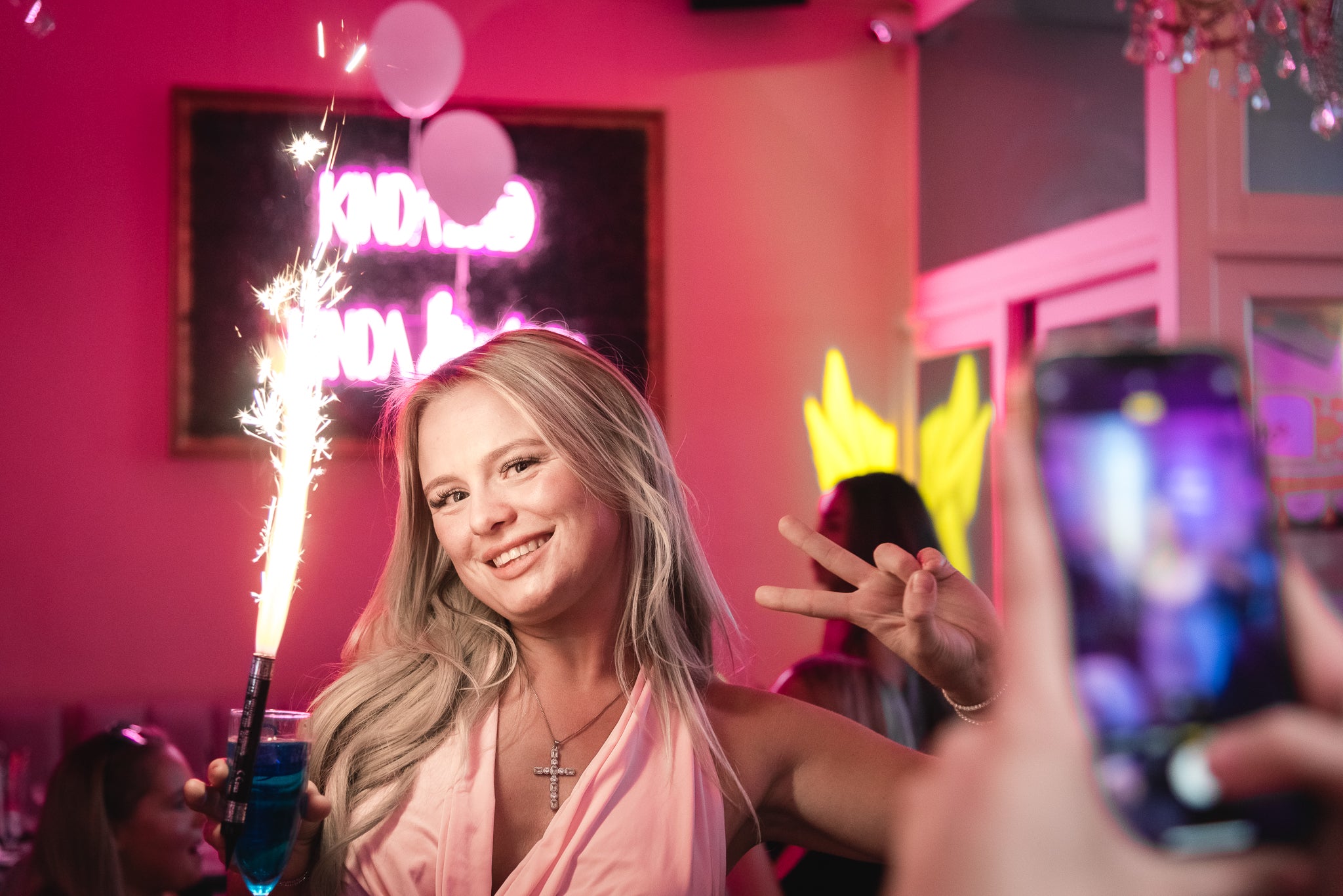 Woman holding a sparkler in a pink-themed room with people taking photos at her birthday at lovebrunch