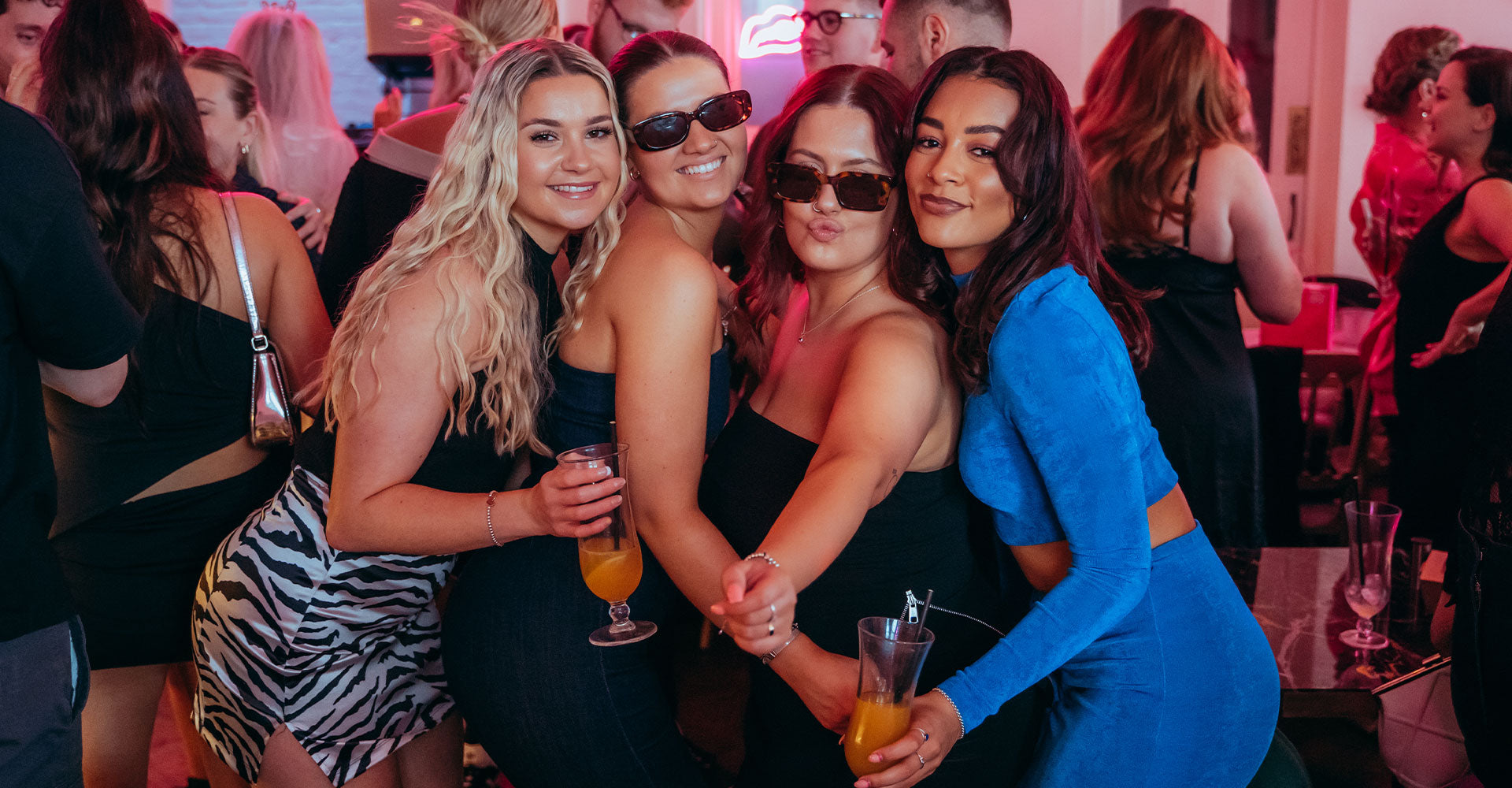Three women posing together at a social event with drinks in hand.