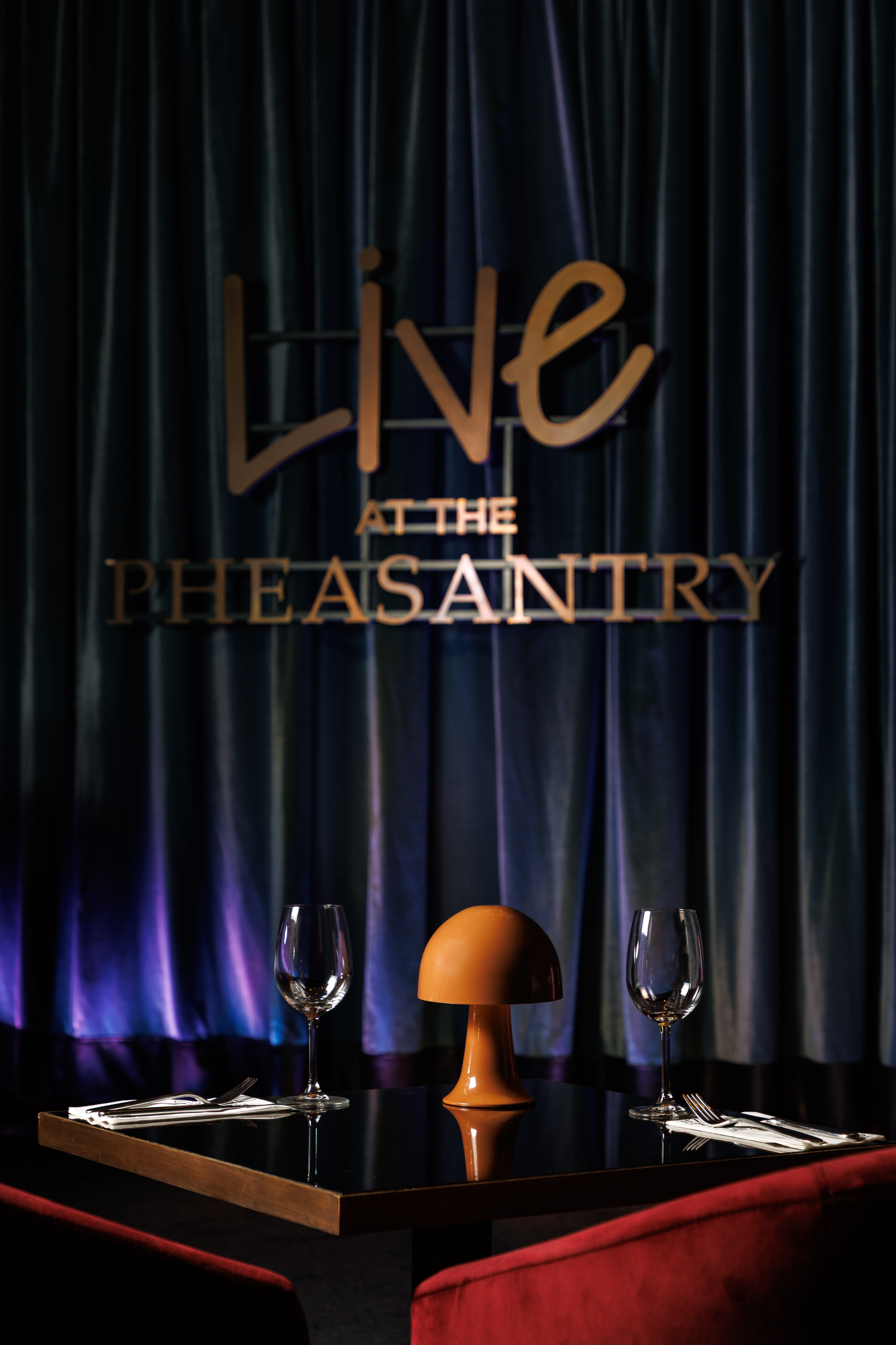 Dining setup with 'Live at The Pheasantry' sign on a dark curtain background